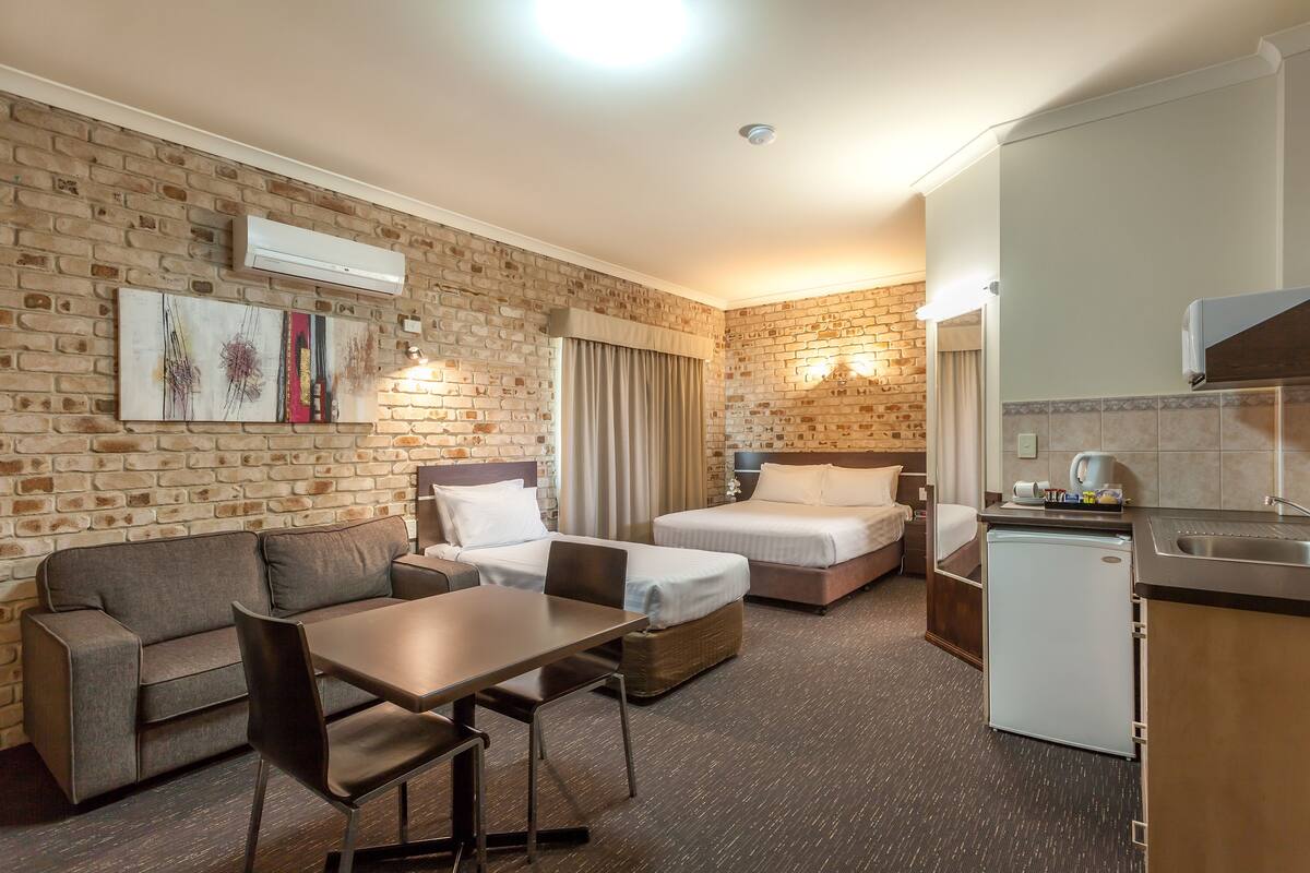 A hotel room with a brick wall, a sofa, a bed, a desk, and a kitchenette.