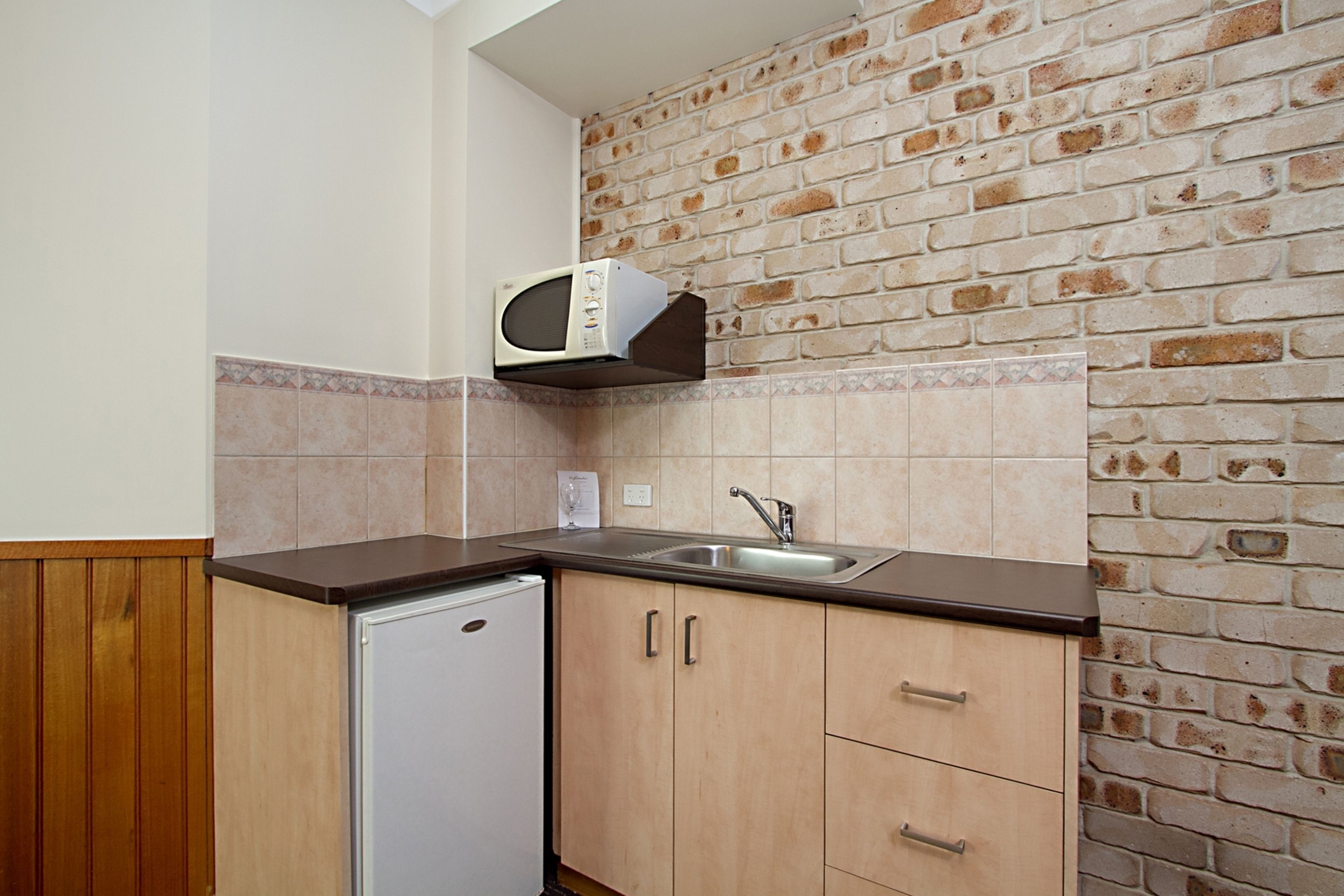 Una cucina compatta con forno a microonde, lavello e pensili in legno, con una parete in mattoni.