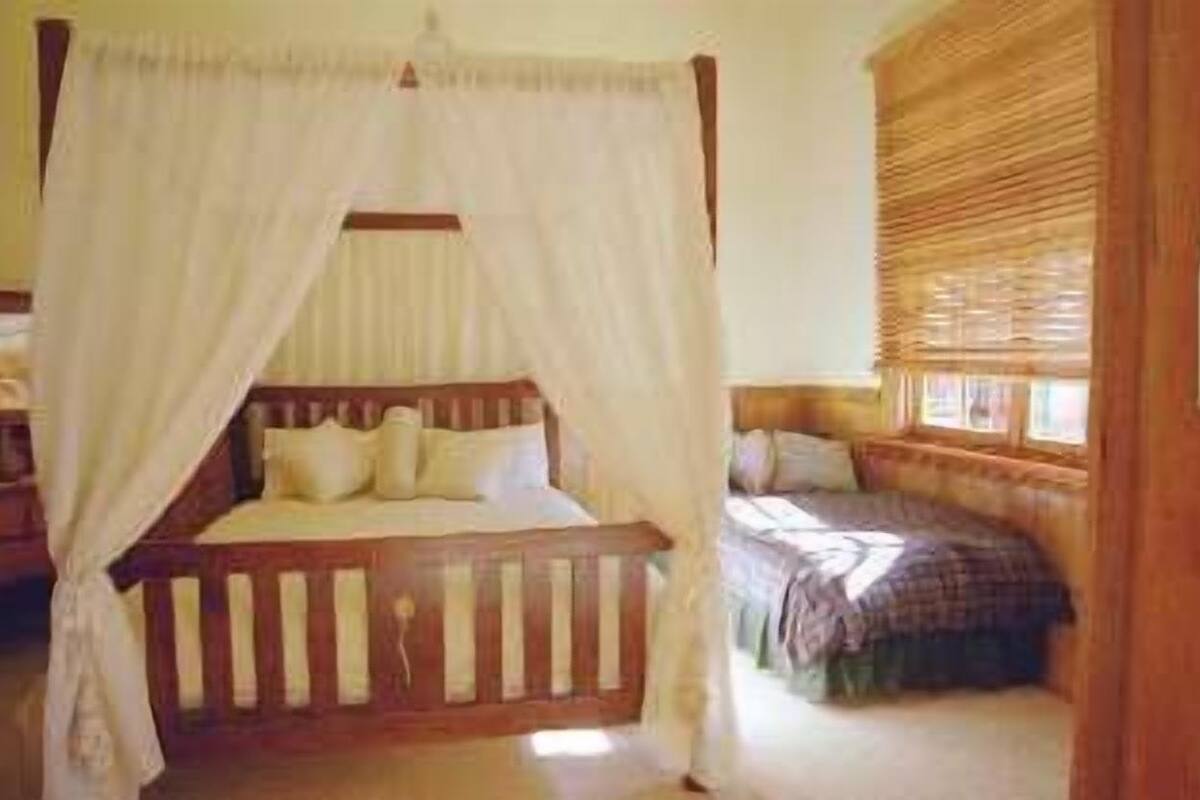 A bedroom with a four-poster bed, a wooden headboard, and a window with blinds.