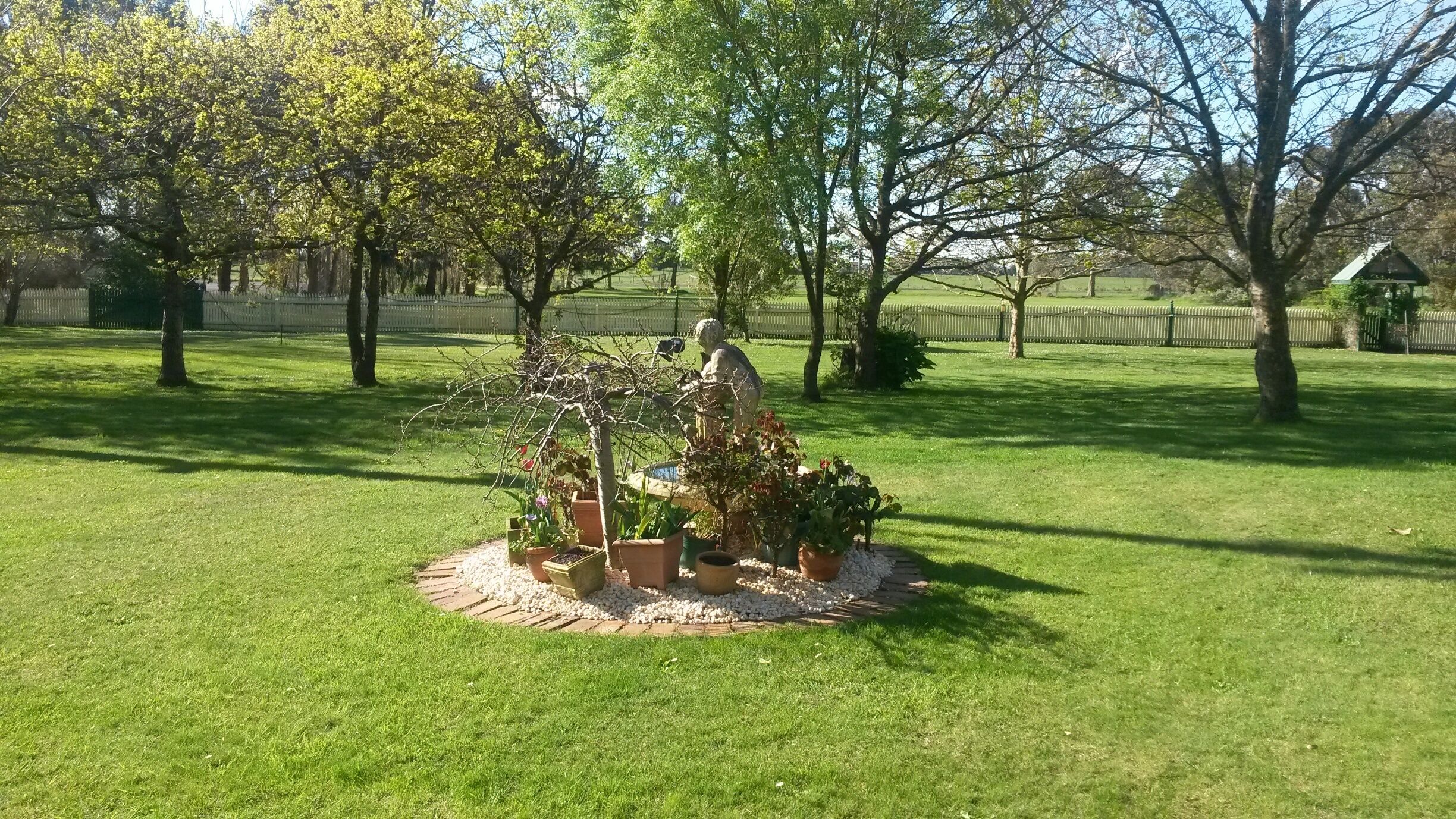 A well-maintained garden with a central sculpture, surrounded by various potted plants and a brick pathway.