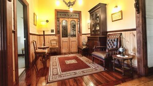 A traditional room with wooden flooring, a red rug, a chandelier, a wooden cabinet, and two leather chairs. - Butterfly Farm (Nirranda)