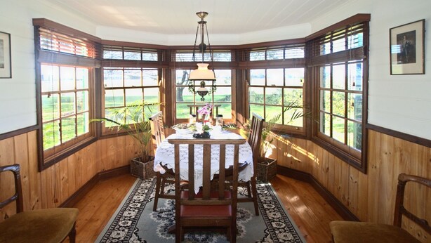 A dining area with a table set for two, surrounded by wooden paneled walls and large windows offering a view of the outdoors. - Butterfly Farm (Nirranda)