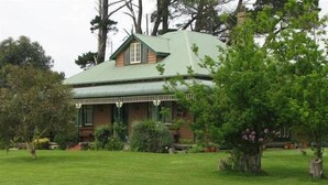 A two-story house with a green roof and a porch. - Butterfly Farm (Nirranda)