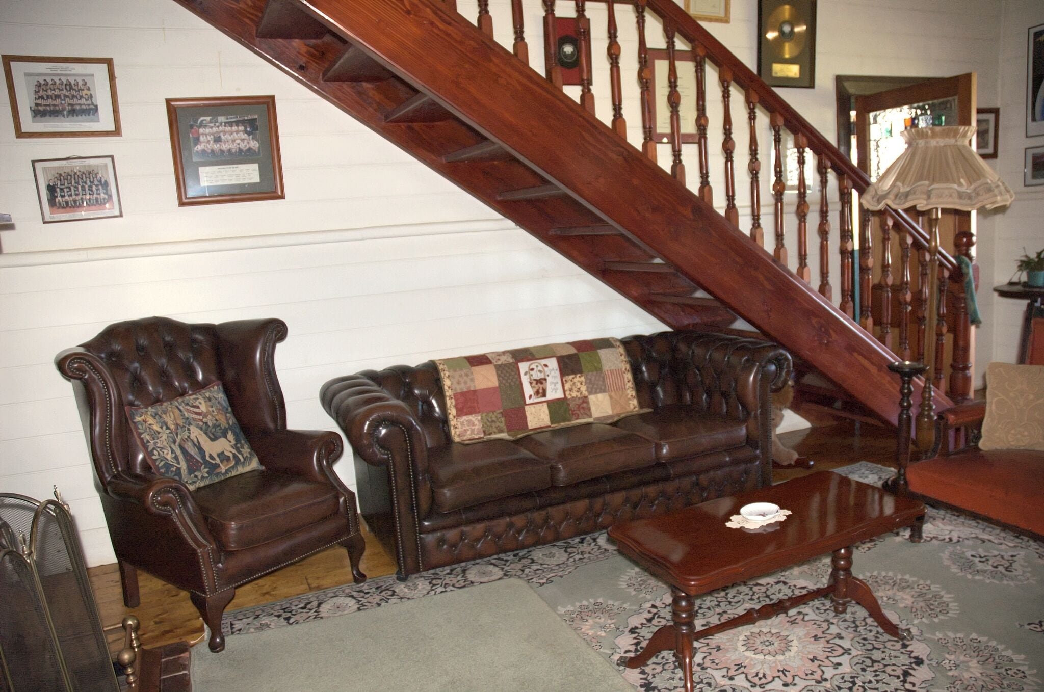 A traditional living room with a wooden staircase, a leather armchair, a sofa, and a coffee table.