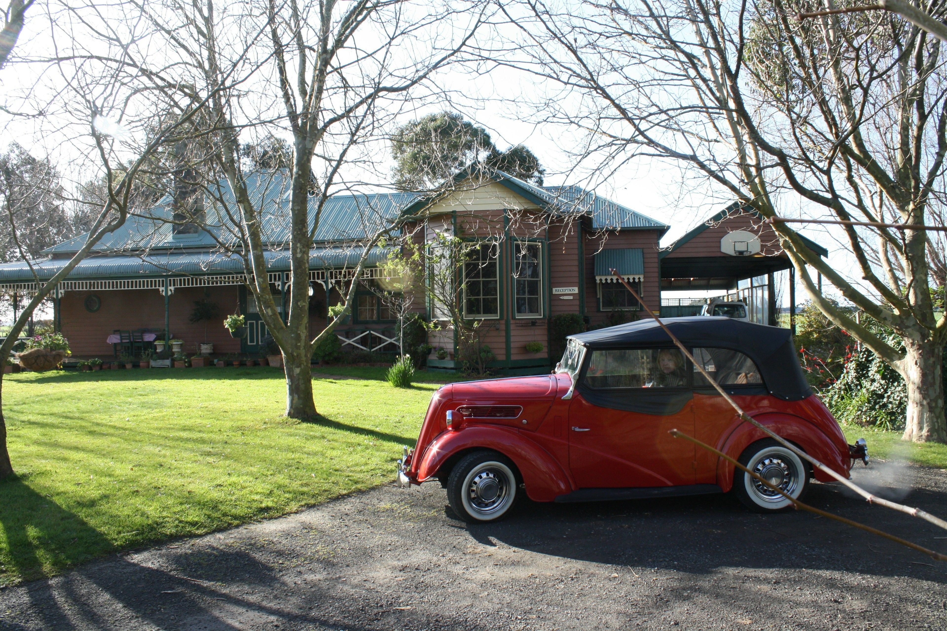 A vintage red convertible car parked in front of a building with a green roof and a sign that reads "RECEPTION".