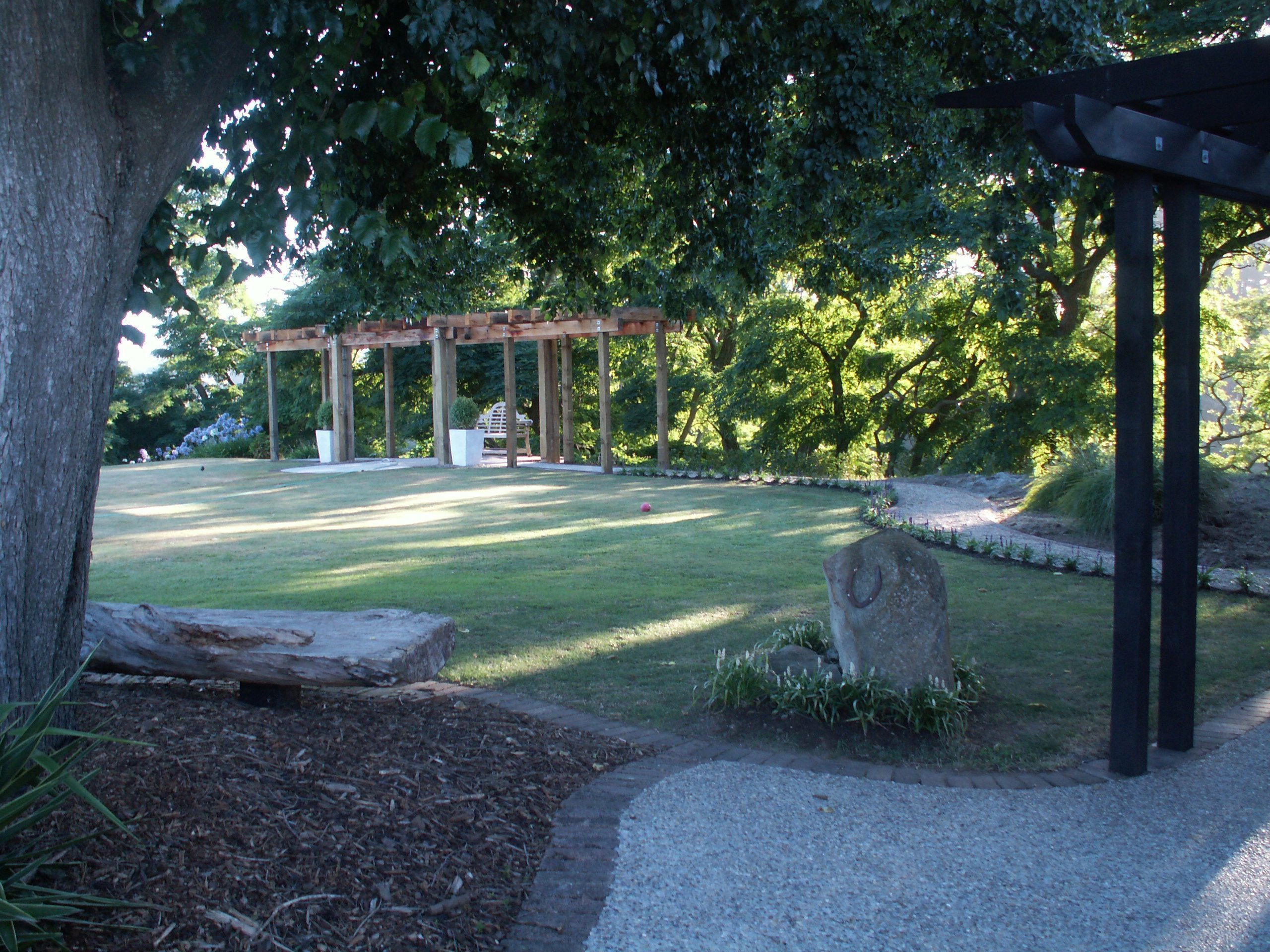 A park with a pergola, a stone bench, and a gravel path.