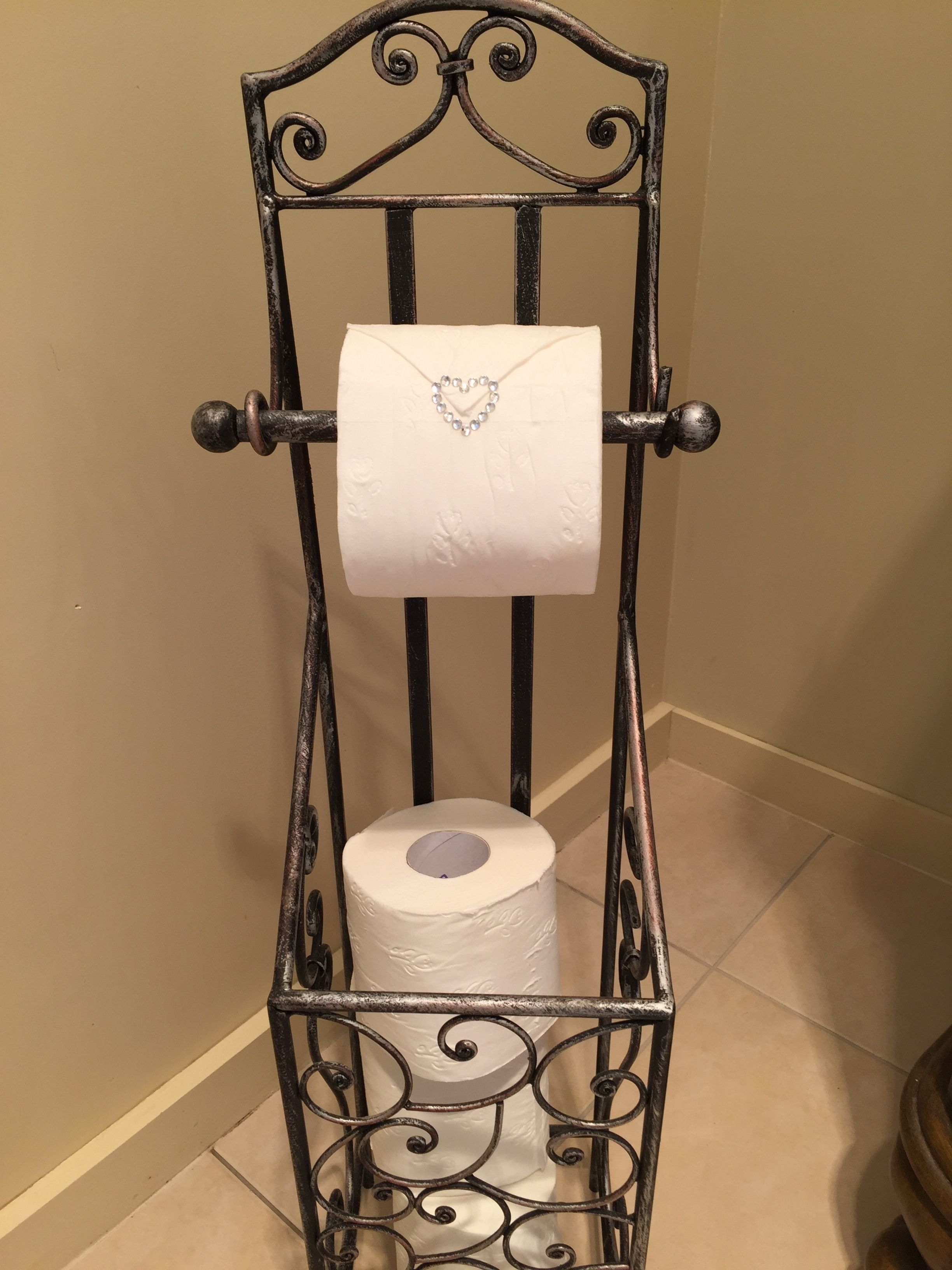 A metal toilet paper holder with a decorative heart-shaped embellishment.