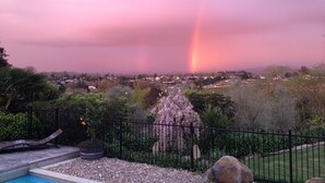A residential area with a swimming pool, a garden with a fence, and a view of a rainbow in the distance. - Cambridge Coach House (Cambridge)