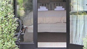 A bedroom with a bed, a chandelier, and a view of greenery outside.