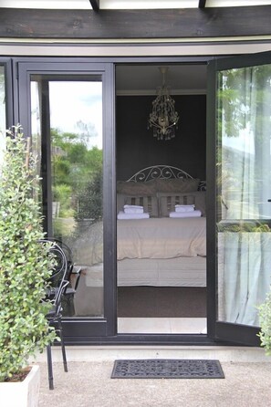 Een slaapkamer met een bed, een kroonluchter en uitzicht op groen.