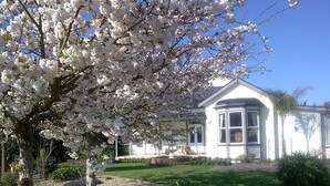 A house with a white exterior, a covered porch, and a well-maintained garden with a large flowering tree. - Cambridge Coach House (Cambridge)