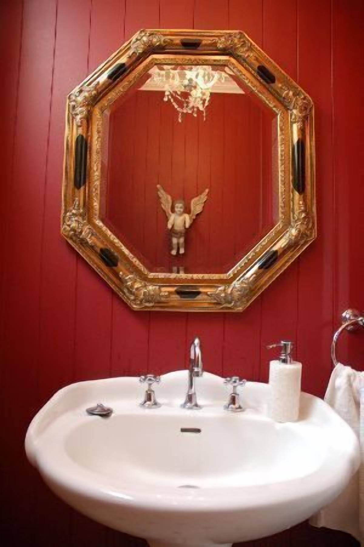 Un baño con un lavamanos blanco, un espejo con marco dorado y una pared roja.