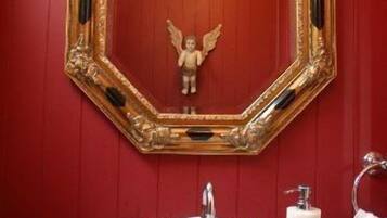 Un baño con un lavamanos blanco, un espejo con marco dorado y una pared roja.