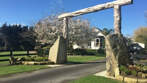 A stone archway with a wooden beam across it, a white house with a black roof, and a tree with white blossoms in the background. - Cambridge Coach House (Cambridge)