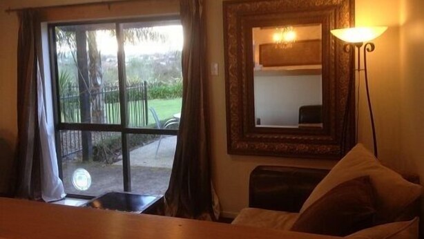 A room with a large window, a mirror, a lamp, and a bed.
