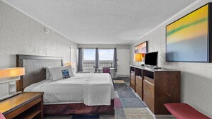 A hotel room with a large bed, a desk, a TV, and a balcony with a view. - Oasis Hotel (North Myrtle Beach)