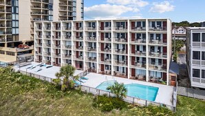 A multi-story hotel with balconies, a swimming pool, and a parking area. - Oasis Hotel (North Myrtle Beach)