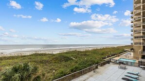 A beachfront view from a balcony with a pool and lounge chairs. - Oasis Hotel (North Myrtle Beach)