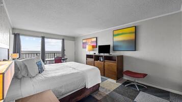 A hotel room with a bed, a desk, a TV, and artwork on the wall.