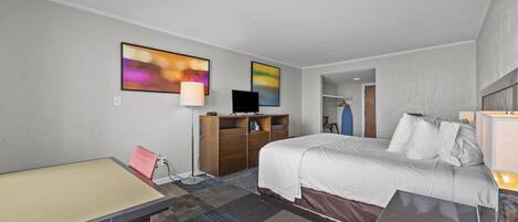 A hotel room with a bed, a desk, a chair, a TV, and a wardrobe.