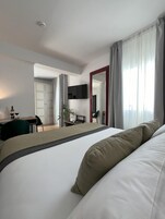 Una habitación de hotel moderna con una cama grande, un escritorio con silla, un televisor montado en la pared y una ventana con cortinas.