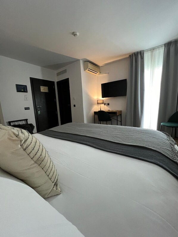 Habitación de hotel con cama, escritorio, silla, televisor y ventana con cortinas.
