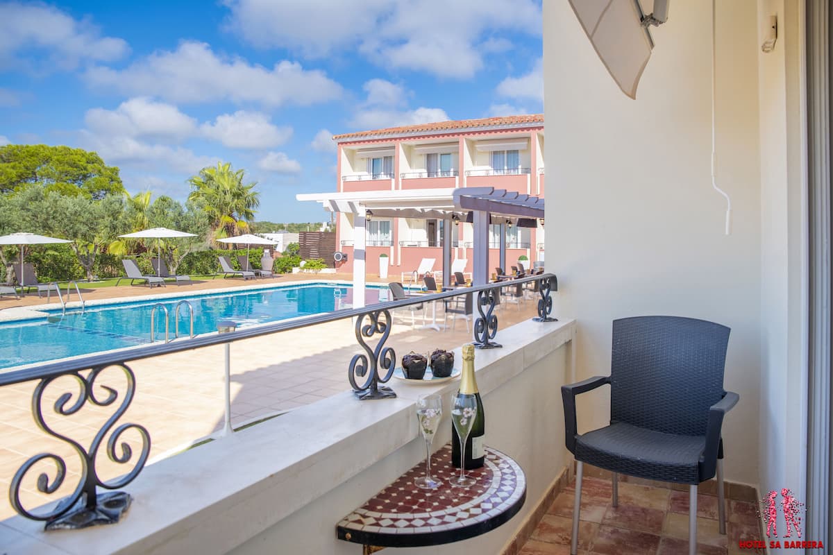 Un balcon avec vue sur la piscine, une chaise, une bouteille de champagne et une table carrelée.