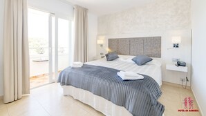 Una habitación de hotel moderna con una cama grande, una mesita de noche, una lámpara de pared y vistas a través de un ventanal corredero.