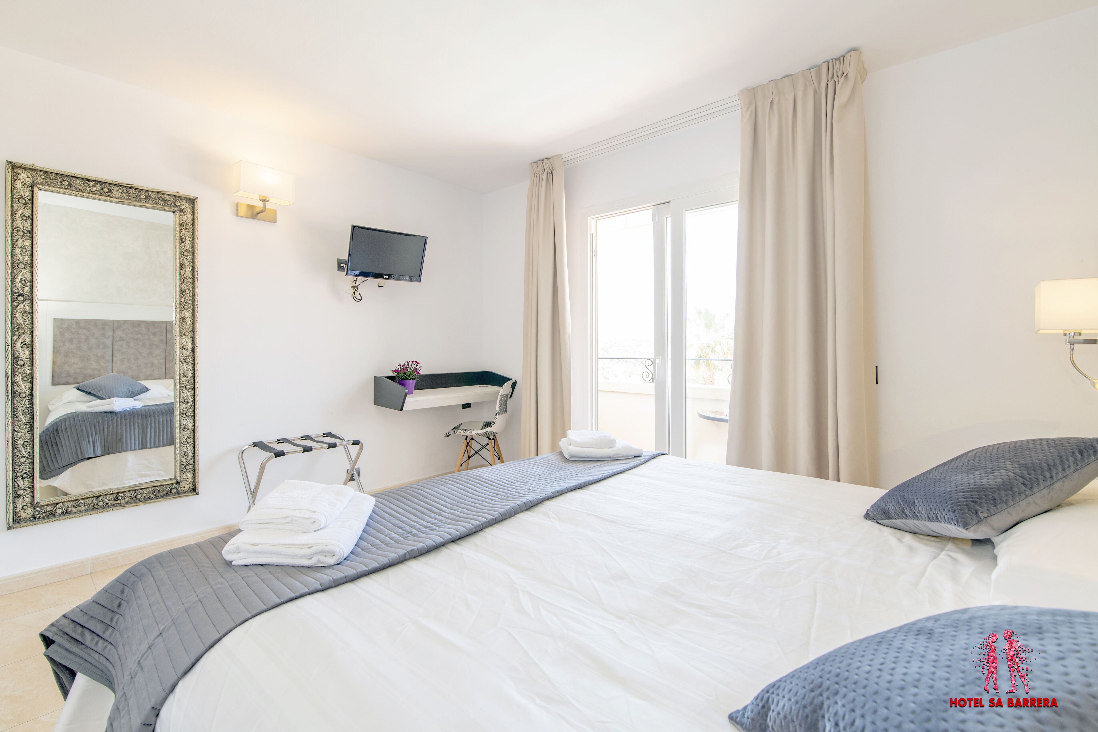 Ein Hotelzimmer mit einem großen Bett, einem Fernseher, einem Spiegel, einem Fenster mit Vorhängen und Balkonblick.