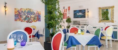A dining area with multiple tables, colorful chairs, and a large plant.