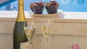 Vista de la piscina con una botella de champán, dos copas y dos cupcakes sobre una mesa.