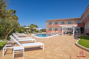 A hotel pool area with sun loungers, a swimming pool, and a building with balconies.