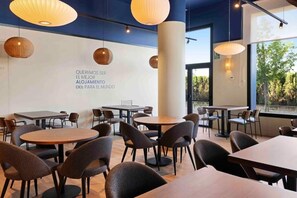 A modern dining area with round tables and chairs, large hanging lights, and a wall with text. - B&B Hotel Albacete  (Albacete)
