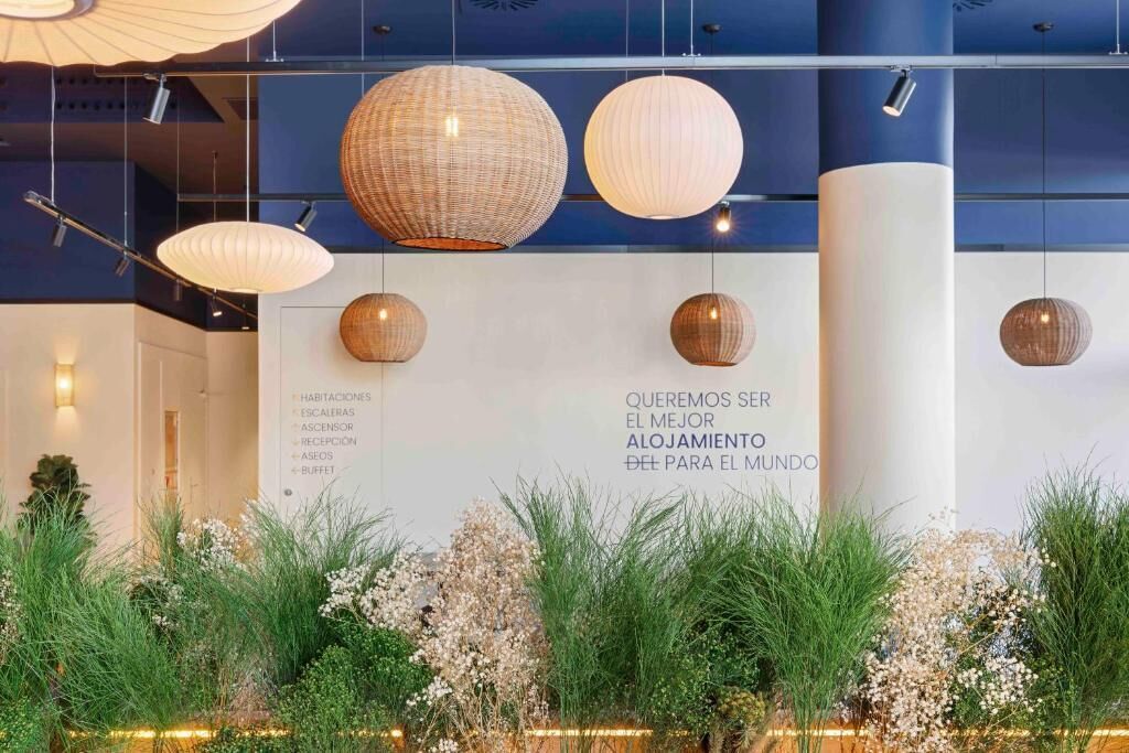 A hotel interior with hanging spherical light fixtures, a white wall with text, and a reception area.