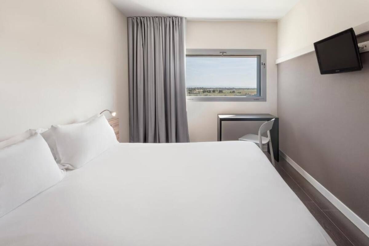A hotel room with a bed, a desk, a chair, a TV, a window, and a curtain.