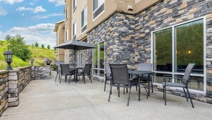 An outdoor patio with stone walls, a table with chairs, and a large window.