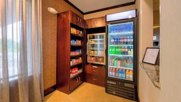 Habitación de hotel con minibar, un refrigerador lleno de bebidas y un mueble de madera con aperitivos.