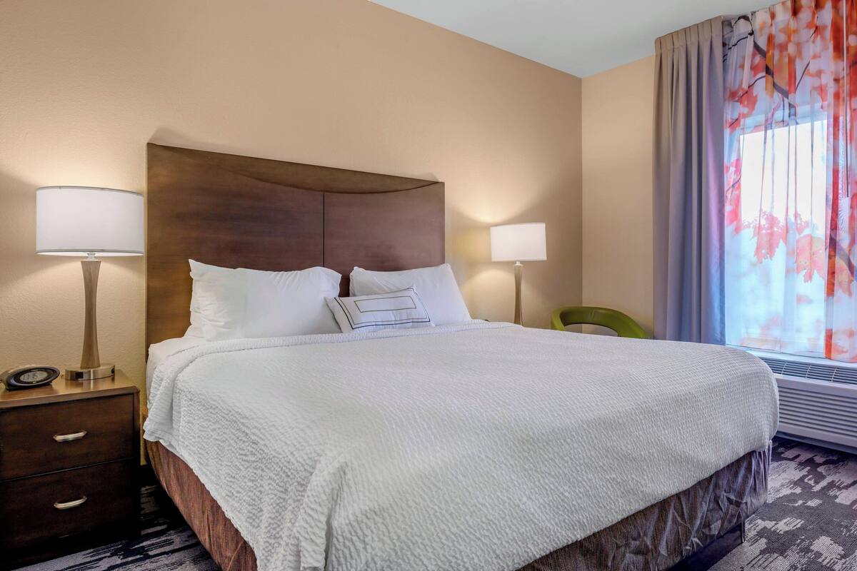 A hotel room with a large bed, two bedside lamps, a nightstand, and a window with curtains.