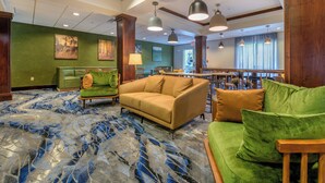 A lobby with a green sofa, a beige sofa, and a green armchair. There are pendant lights, a patterned carpet, and a reception desk in the background.