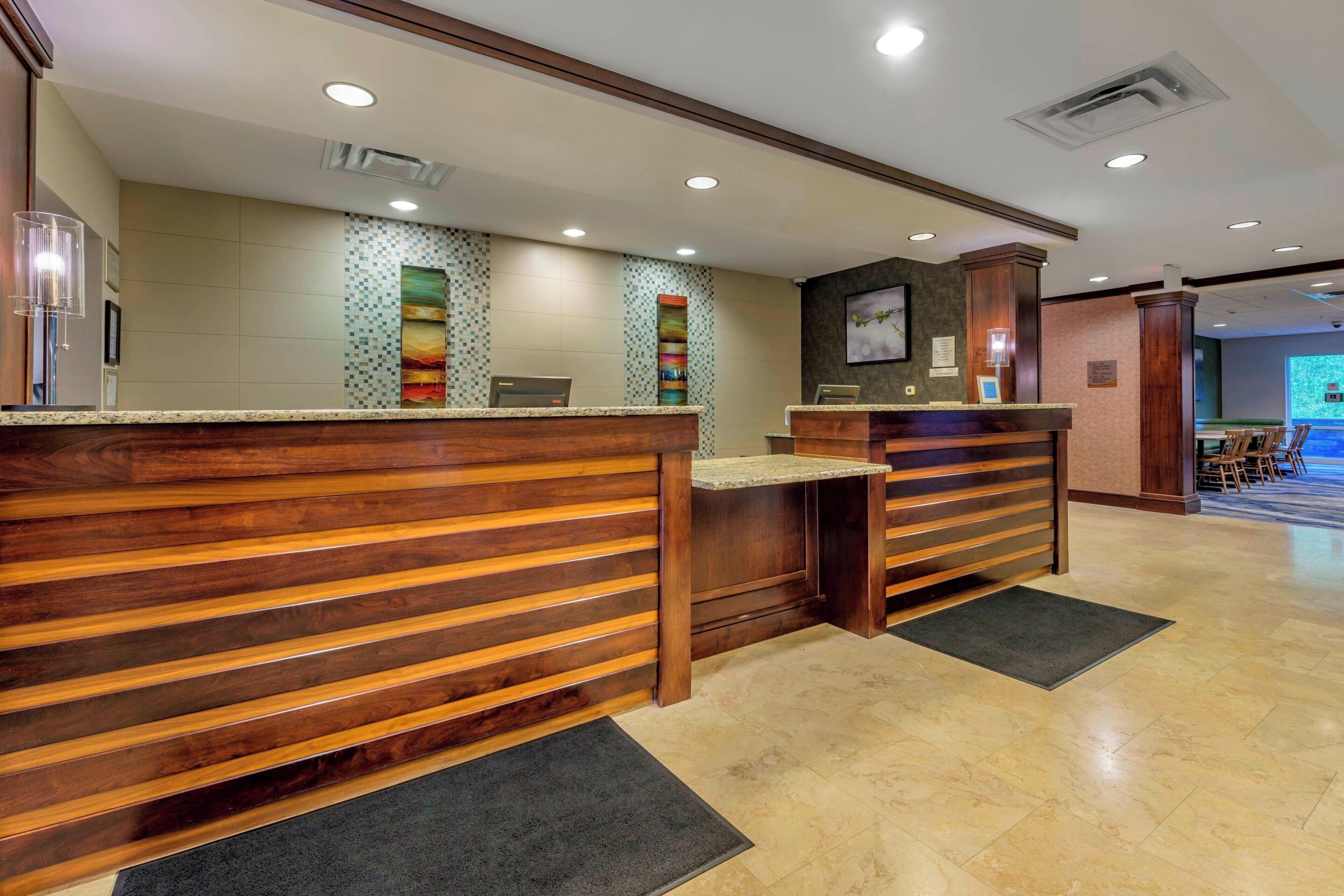 A reception area with wooden reception desks, a tiled wall with a colorful vertical design, and a projection screen in the background.