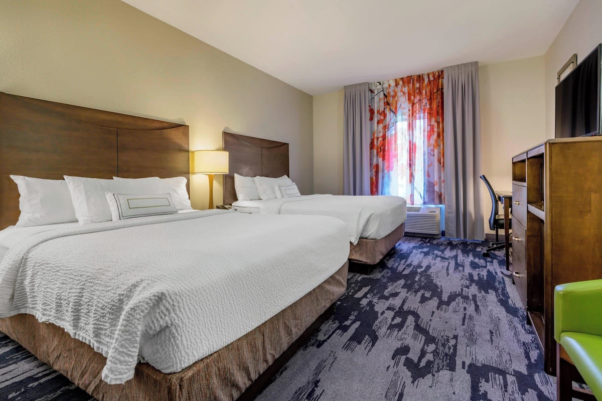 A hotel room with two beds, a desk, a chair, and a TV.