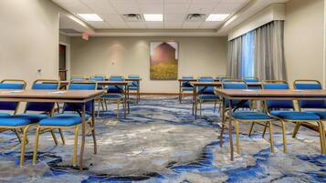 A conference room with blue chairs and tables, a carpeted floor, and a painting on the wall.