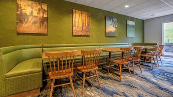 A restaurant with a green booth seating area, wooden chairs, and artwork on the walls.