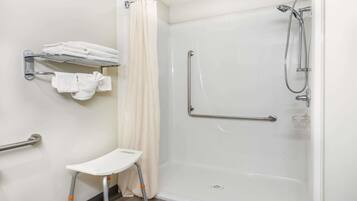 Un baño moderno con ducha a nivel, barras de apoyo, un toallero blanco y un taburete pequeño blanco.