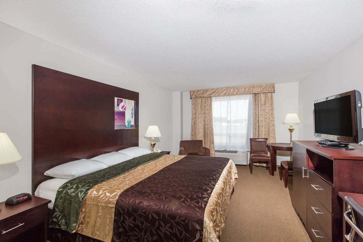 A hotel room with a large bed, a desk with a television, a chair, and a desk lamp.
