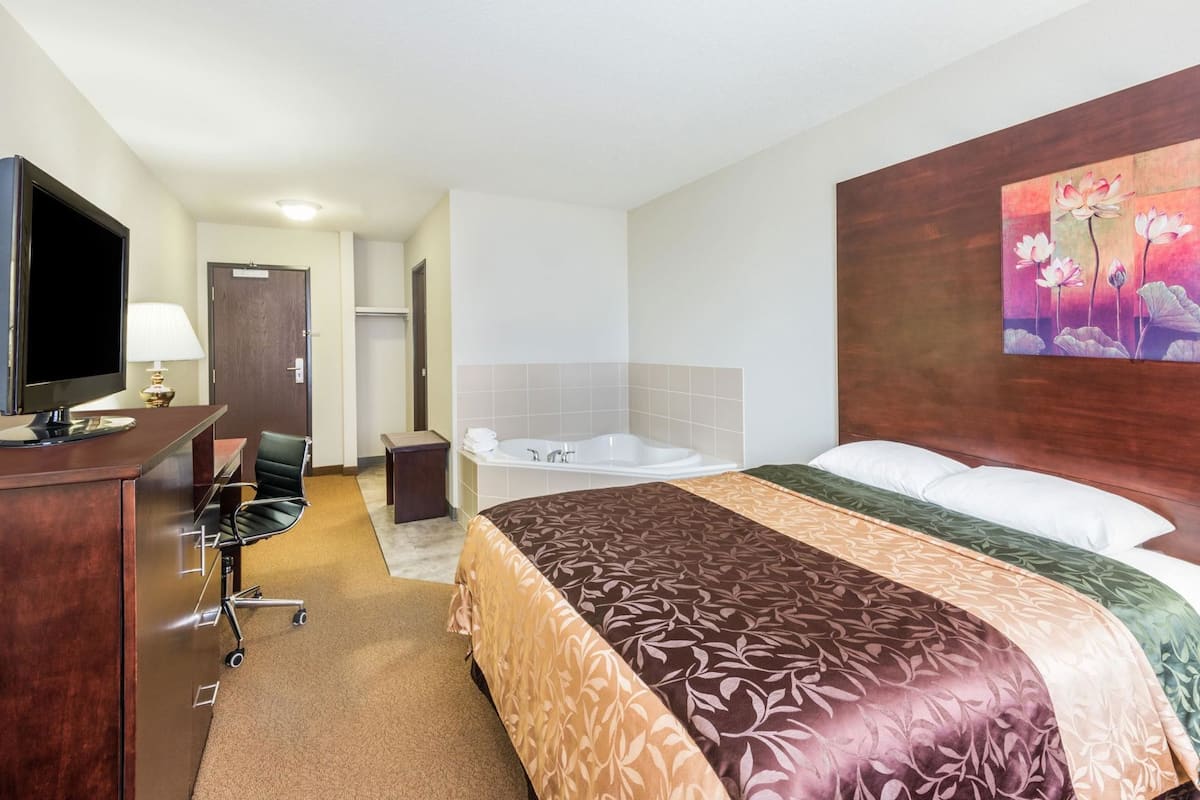 A hotel room with a bed, a desk with a TV, a bathroom with a bathtub, and a painting on the wall.