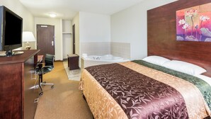 Una habitació d'hotel amb un llit, escriptori amb ordinador, televisió, bany amb banyera i un quadre a la paret.