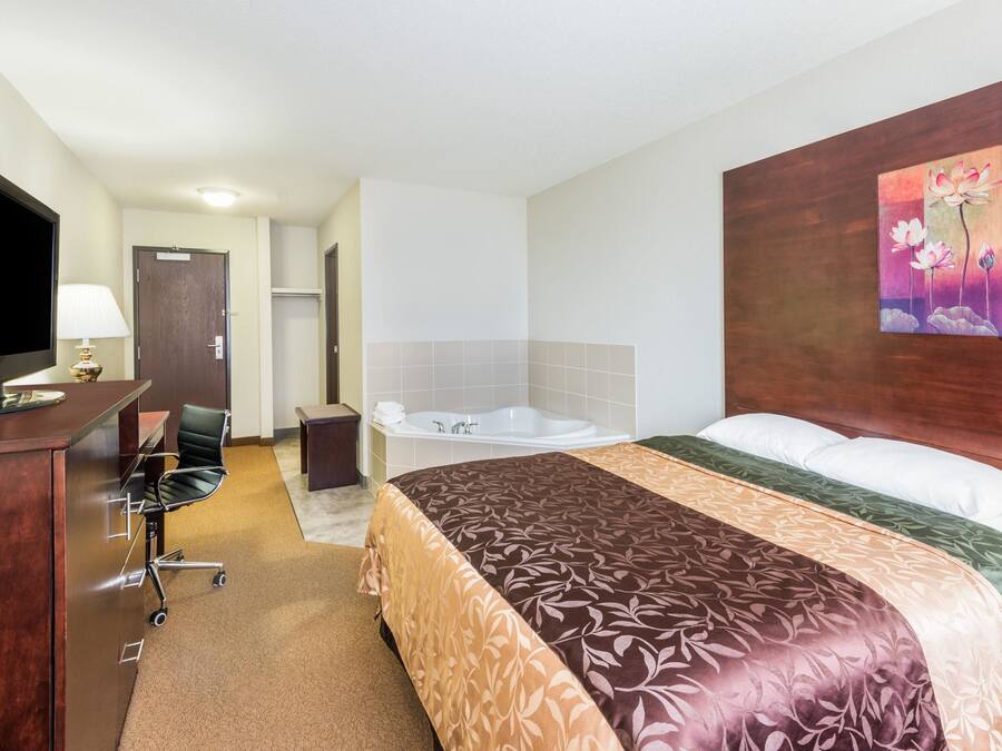 Quarto de hotel com cama, escrivaninha com computador, televisão, banheiro com banheira e um quadro na parede.