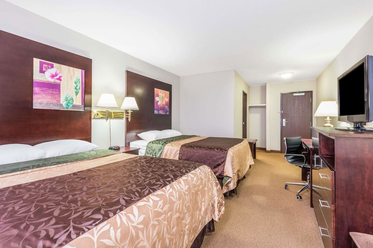 A hotel room with three beds, a desk with a computer, and a television.