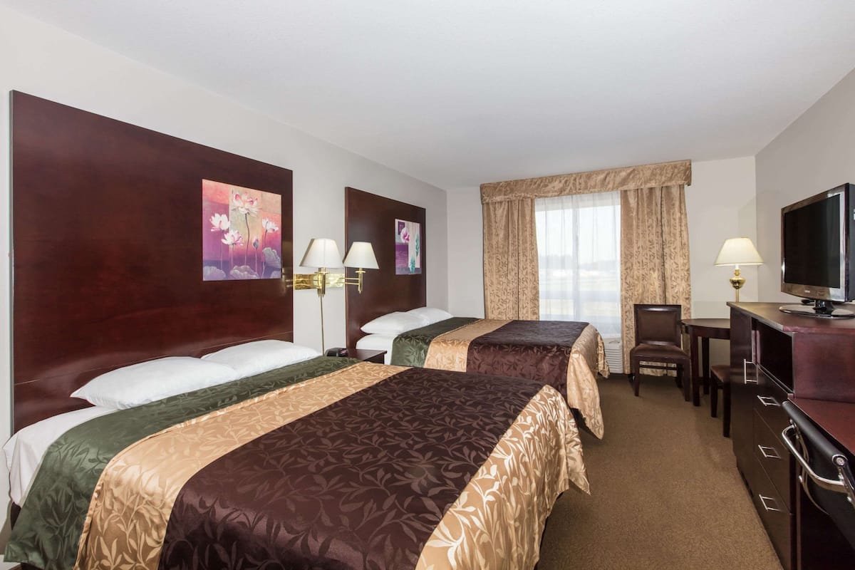 A hotel room with two beds, a desk, a chair, a television, and artwork on the walls.